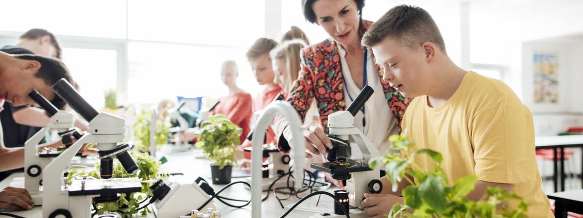 Inclusive practice in a classroom: a teacher helps a boy with Downs syndrome use a microscope